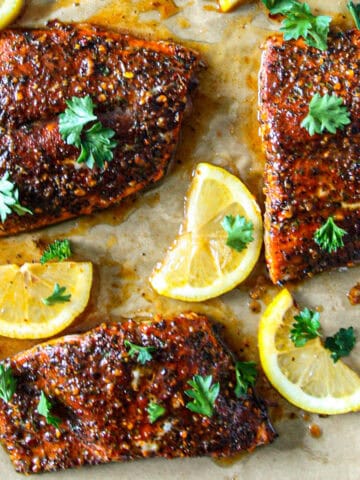 Three Cajun honey butter salmon fillets with lemon wedges.