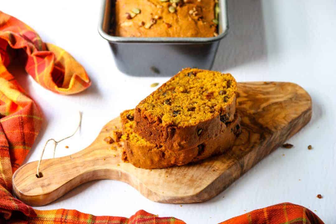 Two thick slices of pumpkin spice loaf stacked on a irregular shaped wood board