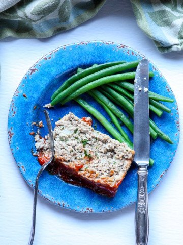 A piece of meatloaf  on a plate with a fork and knife