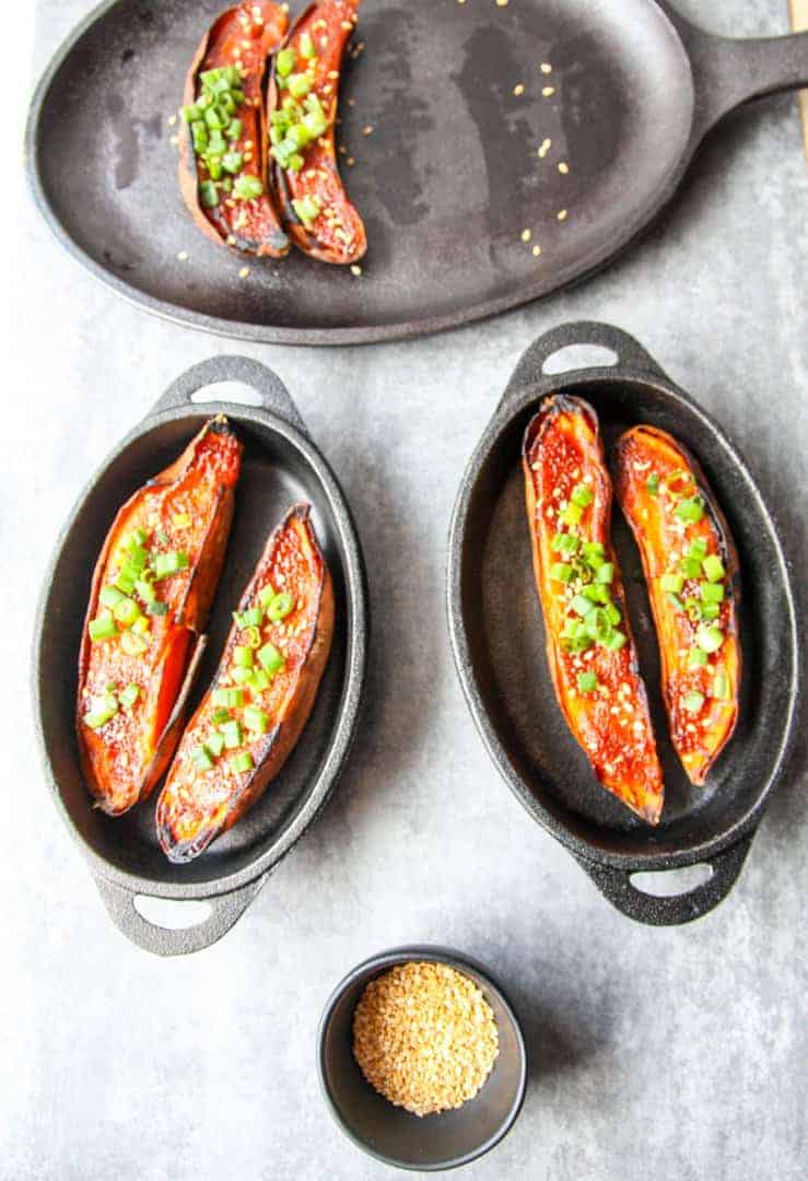 Two cast iron serving dishes, each with two halves of miso baked sweet potatoes