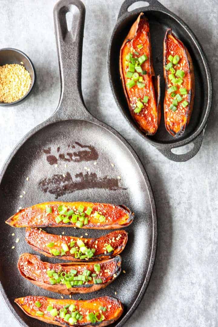 black cast iron pan with 4 miso baked sweet potato halves and a serving dish with two sweet potato halves