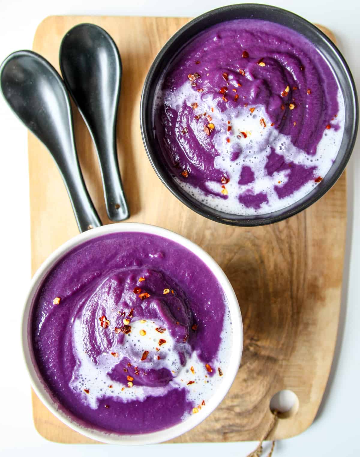 Two bowls of purple cabbage soup, one white bowl and one black bowl. 