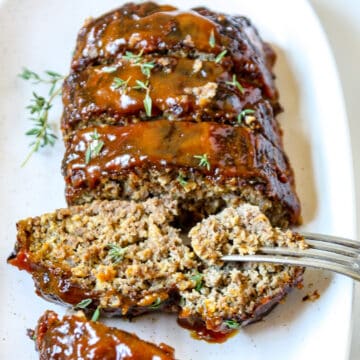 Sliced air fryer meatloaf on a white plate with a fork taking a piece of one slice.