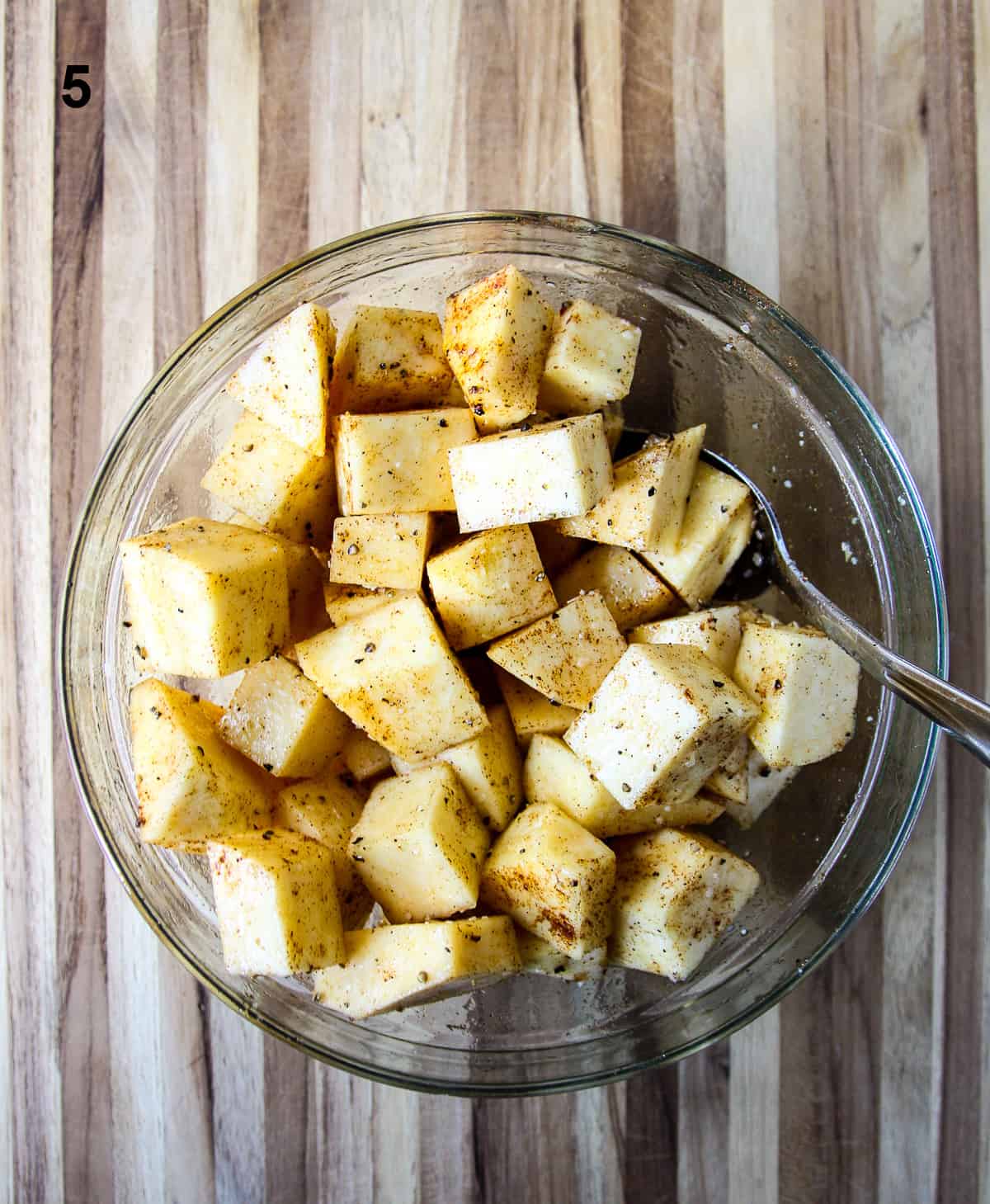 The cut  cubes being tossed with seasoning and oil in a glass bowl.