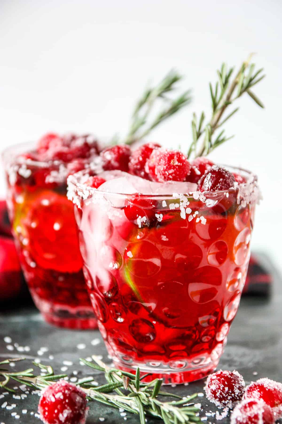 Two glasses of mistletoe margaritas garnished with sugared cranberris and rosemary.