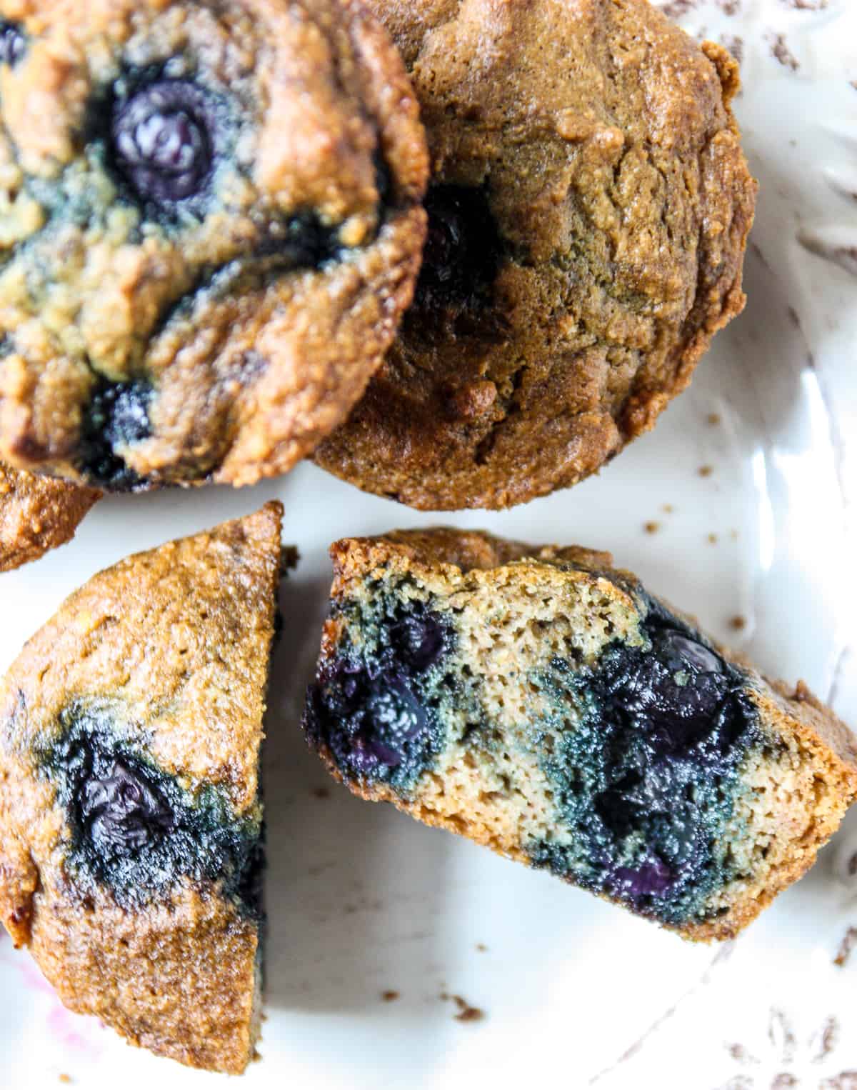 Blueberry muffins on a white plate with one of them cut in half.

