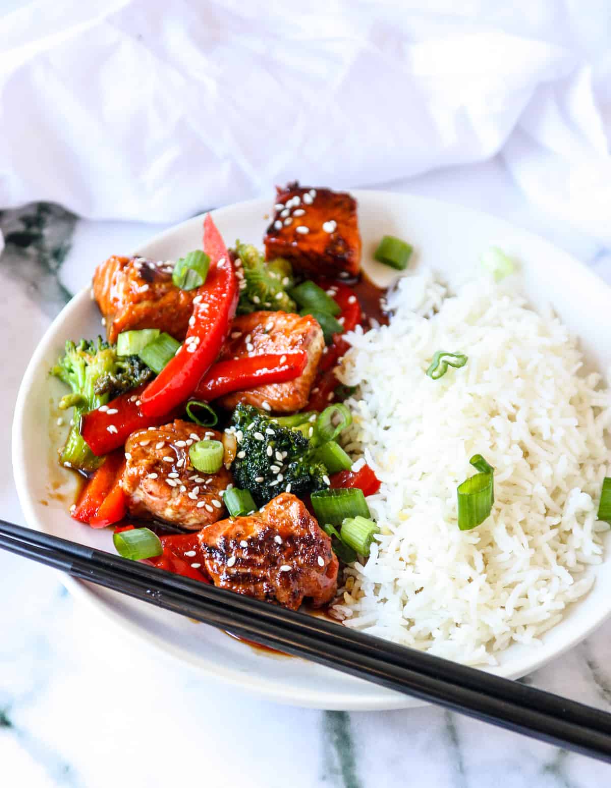 Salmon stir fry and white rice on a white plate.