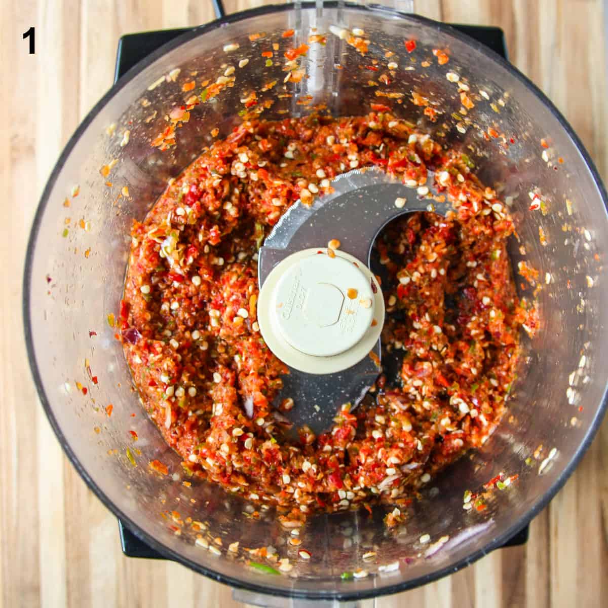 The finely chopped ingredients,  except the vinegar, in the bowl of a food processor.