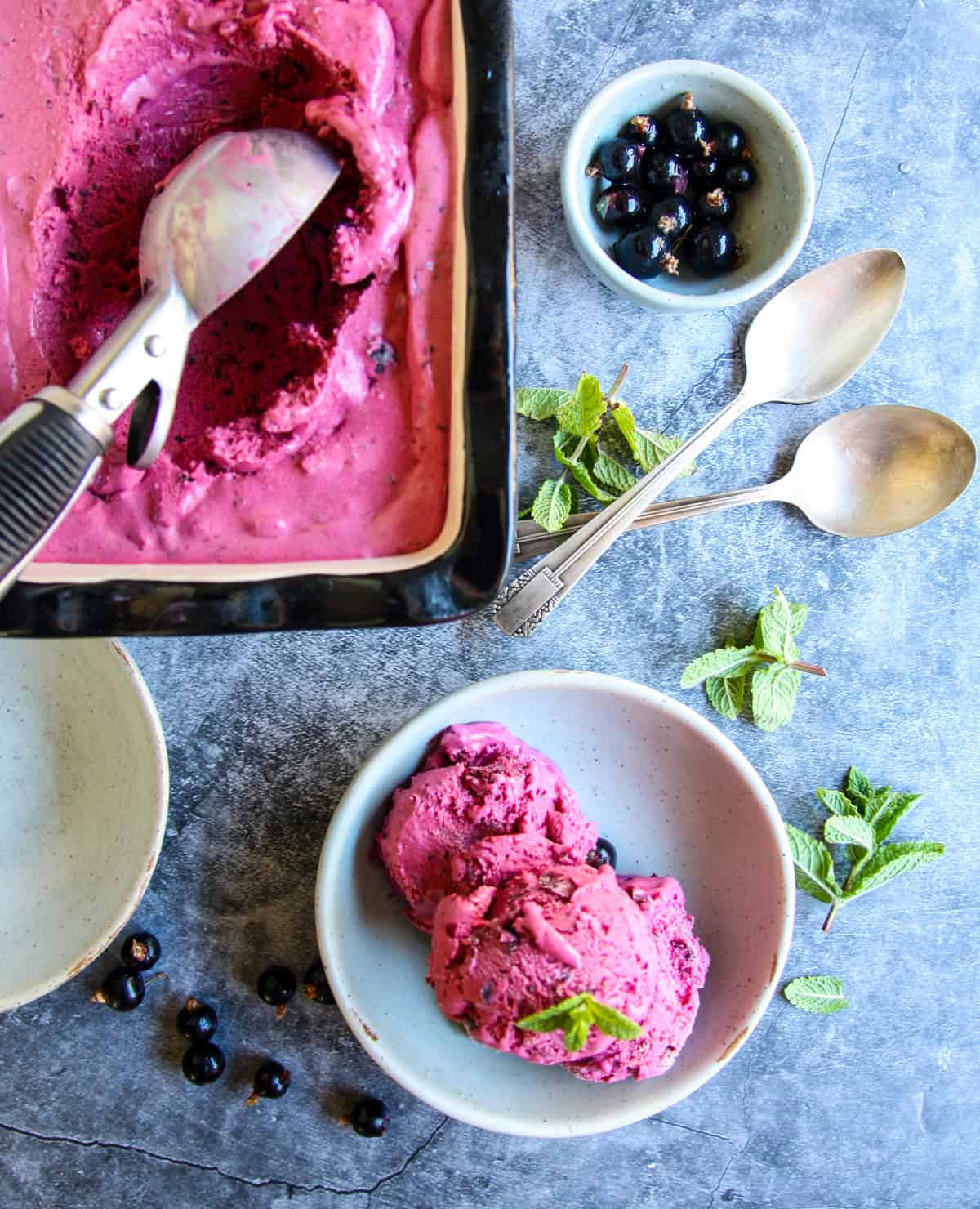 An ice cream scoop in a pan of black current ice cream.